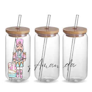 May include: Three glass jars with bamboo lids and clear straws. The jar on the left has a colorful illustration of a nutcracker playing a drum. The middle jar has the name "Amanda" written in cursive. The jar on the right is empty.