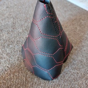 Op de afbeelding: Zwarte leren versnellingspookhoes met rode stiksels in een honingraatpatroon.