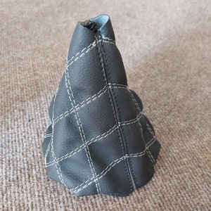 Könnte beinhalten: Schwarzer Lederschalthebelmanschette mit weißen Nähten in Rautenform.