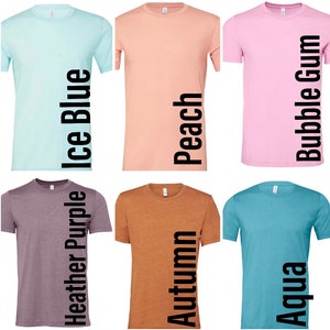 May include: Six different colored t-shirts with the color names printed vertically on the right side of each shirt. The colors are ice blue, peach, bubble gum, heather purple, autumn, and aqua.