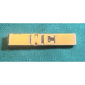 May include: A gold-toned metal tie bar with the letters "WC" in a block letter style. The tie bar is rectangular and appears to be new, possibly still in its original packaging. The background is a teal fabric.