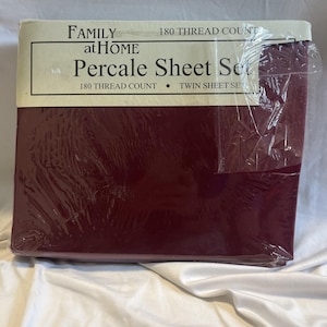 May include: A burgundy percale sheet set, packaged in clear plastic. The packaging features the text "FAMILY at HOME" and "Percale Sheet Set". The label also indicates a 180 thread count and that it is a twin sheet set.
