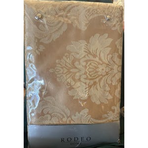 May include: A packaged beige damask tablecloth with a floral pattern. The tablecloth is in a clear plastic wrapping. The brand name "RODEO HOME" is visible on the bottom of the package.