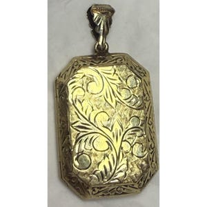 May include: A gold-colored rectangular locket with an ornate floral design. The locket has a decorative bail for a chain and features detailed engraving across its surface. The overall design is vintage and elegant.