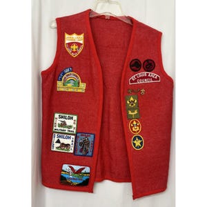 May include: A red vest with multiple patches, including "Junior League Training Camp" and "St. Louis Area Council." Patches feature text like "Shiloh Military Trail" and various emblems. The vest is displayed on a hanger.