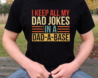May include: A black t-shirt with a vintage-style graphic that reads "I keep all my dad jokes in a dad-a-base".