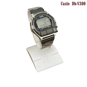 May include: Casio Db-V300 digital watch with a black and silver band, displayed on a white stand. The watch face shows the time and timer functions. The watch has buttons labeled "REC" and "PLAY".