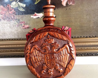 Peut inclure: Une bouteille en bois avec un aigle sculpté et le mot "SRBIJA" sur le devant. La bouteille est ornée d'un ruban rouge et blanc autour du cou.