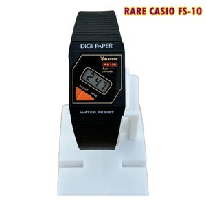 Puede incluir: Un reloj digital Casio FS-10 negro con correa estriada. La esfera muestra el texto DiGi PAPER, el logotipo de Playboy, FS-10, Auto calendar y WATER RESIST. Un botón triangular naranja está situado en el lado izquierdo de la pantalla digital.