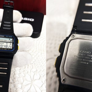 May include: Black digital wristwatch with a yellow and blue trim. The watch face displays the date, day of the week, and time. The watch back is stainless steel and says "CASIO FT-100W STAINLESS STEEL BACK WATER RESISTANT JAPAN M".