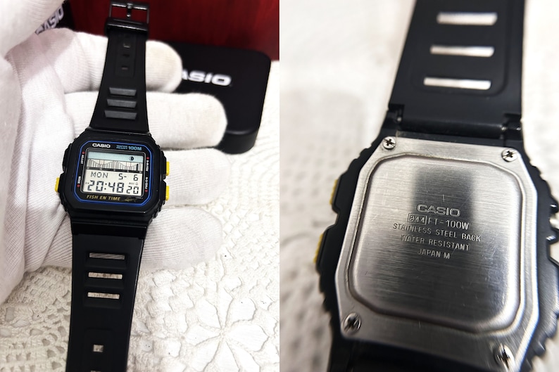 May include: Black digital wristwatch with a yellow and blue trim. The watch face displays the date, day of the week, and time. The watch back is stainless steel and says "CASIO FT-100W STAINLESS STEEL BACK WATER RESISTANT JAPAN M".
