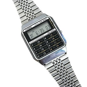 May include: A vintage Casio CA-602 digital watch with a silver-tone metal band. The watch face displays the time as 6:35:03 AM. It features a calculator keypad and the text "ALARM CHRONOGRAPH".