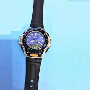 Op de afbeelding: Een zwart en zilveren Casio Pathfinder horloge met een blauwe wijzerplaat en een zwarte rubberen band. Het horloge heeft een digitaal display en een kompas.