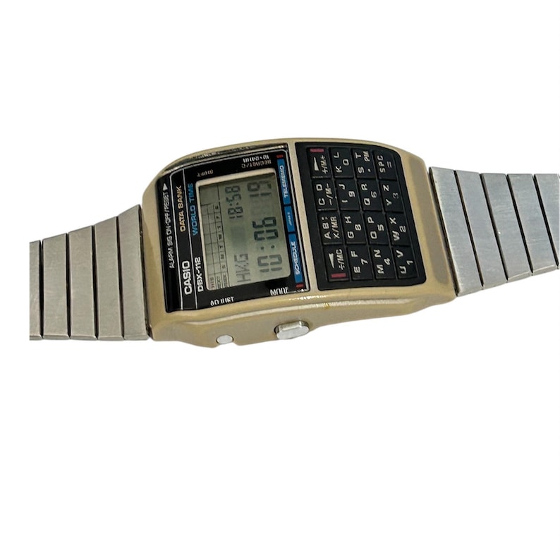May include: A vintage Casio DBX-112 calculator watch with a digital display showing the time. The watch has a beige case, a full keyboard, and a silver-tone metal band. The time displayed is 10:06.