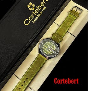 May include: A green leather watch band with a silver watch face. The watch face has a date window and the text "Cortebert Swiss Made 1790" is on the box.