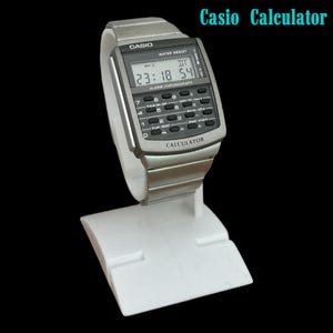 May include: A silver Casio calculator watch with a digital display showing the time. The watch has a calculator keypad and a silver metal band. The text "Casio Calculator" is visible in the image.