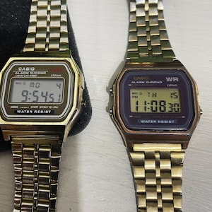 May include: Two gold-tone Casio digital watches with black faces and silver buttons. The watch on the left displays the time as 9:54:51 and the watch on the right displays the time as 11:08:30. Both watches have the text "CASIO" and "ALARM CHRONO" on the face.