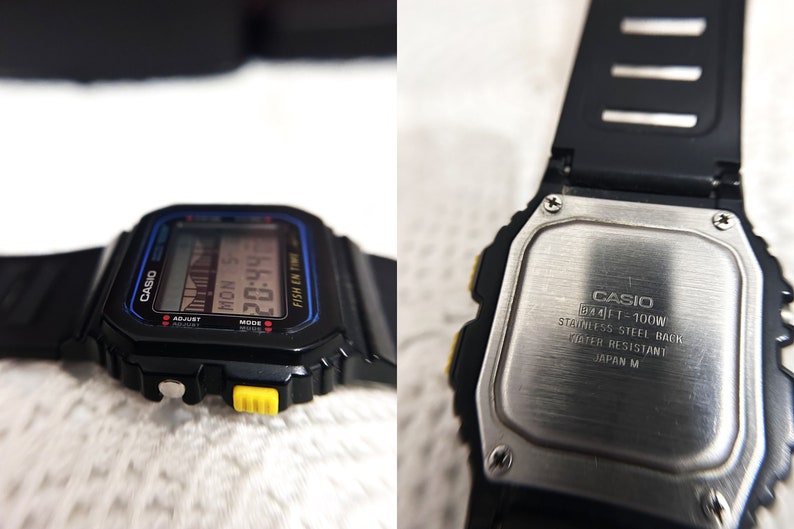 May include: Black Casio digital watch with a blue and yellow trim. The watch face displays the time, date, and day of the week. The back of the watch is made of stainless steel and has the text "CASIO FT-100W STAINLESS STEEL BACK WATER RESISTANT JAPAN M".