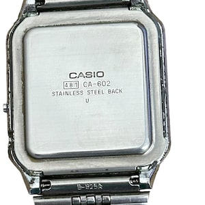 May include: A silver-toned Casio digital watch with a rectangular face and a stainless steel back. The watch band is made of linked metal segments. The watch face displays the Casio brand name and model information.