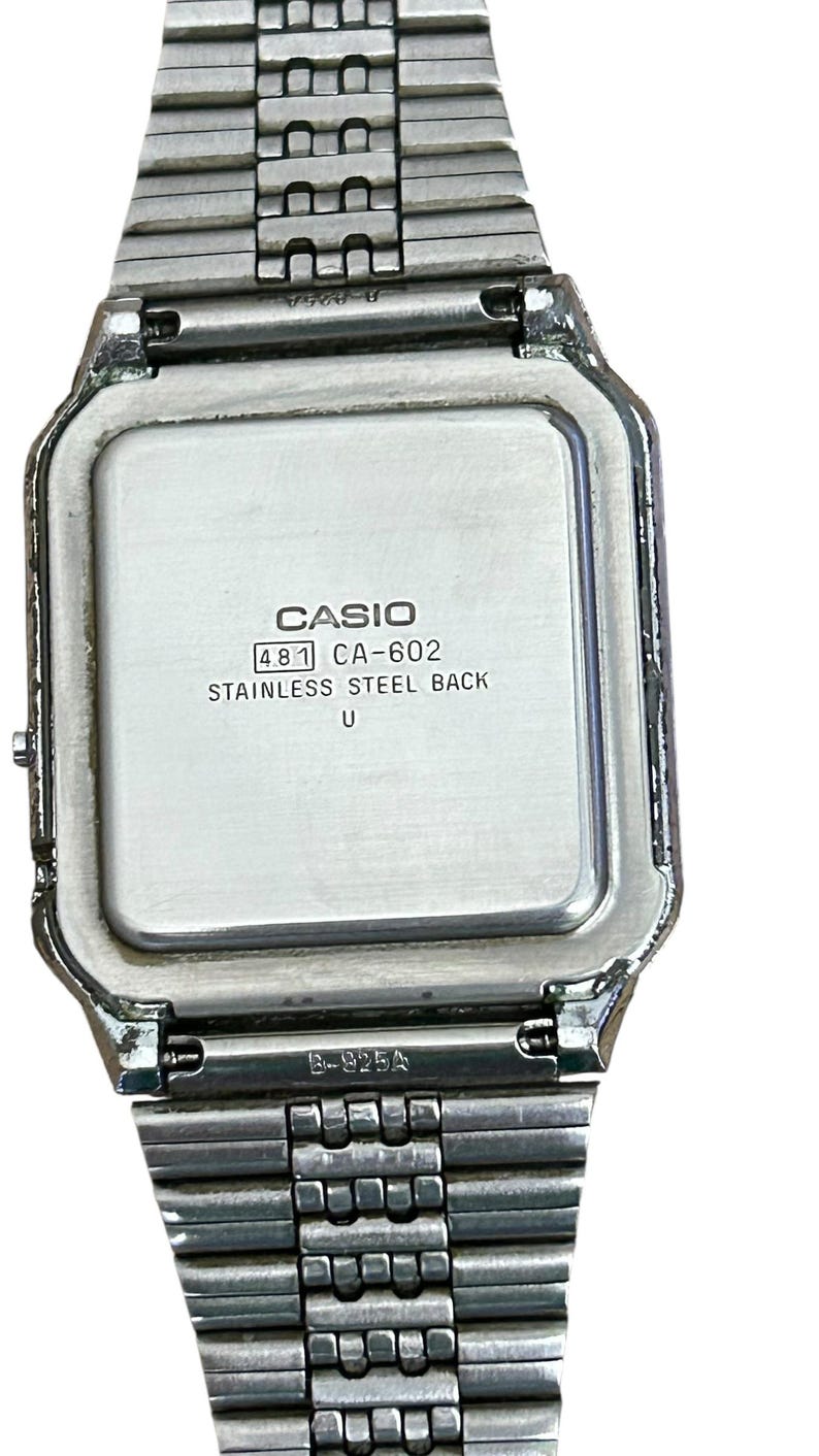 May include: A silver-toned Casio digital watch with a rectangular face and a stainless steel back. The watch band is made of linked metal segments. The watch face displays the Casio brand name and model information.