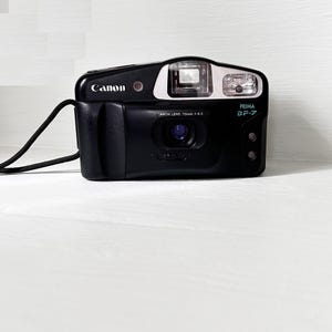 May include: A black Canon Prima BF-7 point-and-shoot film camera with a silver faceplate and a black strap. The camera has a Canon lens, 13mm f/4.5.