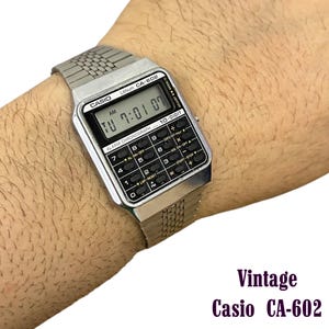 May include: Vintage Casio CA-602 digital watch with a silver-tone metal band and a black and silver face. The watch displays the time as 7:01 AM on Tuesday. The watch has a calculator function and is labeled "10-DIGIT".