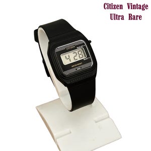 Puede incluir: Reloj digital Citizen negro con una esfera rectangular que muestra la hora 4:28. El reloj tiene una correa negra y está etiquetado como "WATER RESIST" y "JAPAN". El texto "Citizen Vintage Ultra Rare" está encima del reloj.