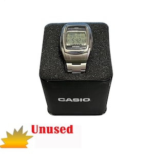 Puede incluir: Un reloj Casio Data Bank plateado con una esfera negra y una correa de acero inoxidable. El reloj está en su caja original, que es negra con el logotipo de Casio impreso en ella. El reloj no se ha usado.