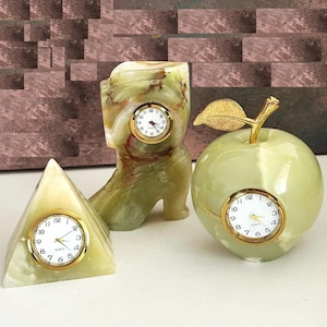 May include: Three green onyx clocks shaped like a boot, an apple, and a pyramid. Each clock has a gold-colored face with black hands and numbers.