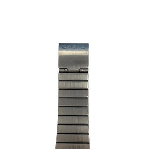May include: Close-up of a silver-toned watch band with the brand name "CASIO" on the clasp. The band is made of rectangular metal links, and the clasp is hinged.
