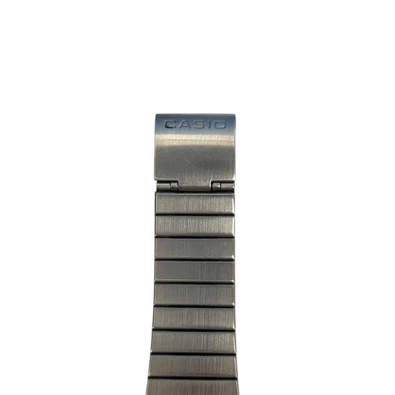 May include: Close-up of a silver-toned watch band with the brand name "CASIO" on the clasp. The band is made of rectangular metal links, and the clasp is hinged.