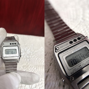 Puede incluir: Un reloj digital Seiko plateado con una pantalla digital negra que muestra la hora y la fecha. El reloj tiene una correa de metal plateada y un bot&oacute;n negro en el lateral.