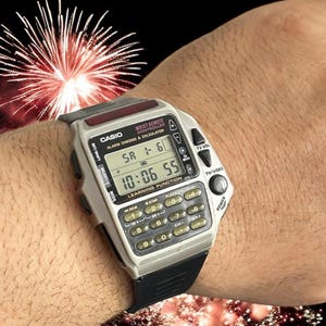 May include: A Casio digital watch with calculator and remote control features. The watch has a silver case, black strap, and a digital display showing the time. It includes buttons for TV volume and channel control. The watch is on a wrist.