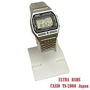Può includere: Un orologio digitale Casio TS-2000 argentato con quadrante nero e cinturino in metallo. L'orologio mostra l'ora, la data e la parola "THERMOMETER". L'orologio è su un espositore bianco. Il testo in basso recita "ULTRA RARE CASIO TS-2000 Japan".