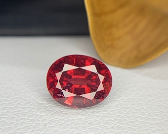 May include: A deep red oval gemstone with facets, set against a white background.