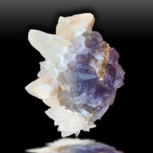 May include: A purple and white fluorite crystal cluster with a natural, rough texture. The crystal is on a black background and has a reflection below it.