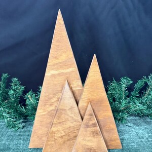 May include: A set of four triangular wooden cutouts arranged in a staggered formation to resemble mountain peaks or trees. The pieces feature a smooth, medium-brown wood grain finish with visible natural textures and sharp, clean-cut edges.