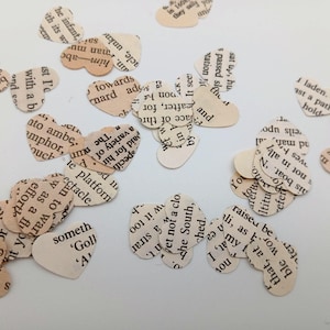 May include: Scattered heart-shaped paper cutouts with text from a book. The paper has a vintage, aged appearance. The text is in black, and the paper is off-white. Ideal for scrapbooking or crafts.