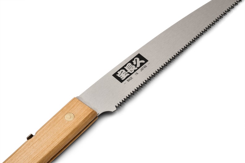 May include: A close-up of a small, folding saw with a wooden handle. The blade is silver and has a serrated edge. The saw is labeled "Silky" in Japanese characters and "Made in Japan".