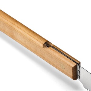 May include: A close-up of a wooden-handled saw with a metal blade. The handle is made of light-colored wood and has a small brass pin near the blade.
