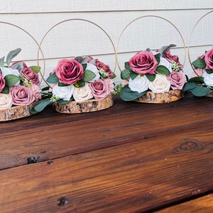 May include: Four rustic wooden centerpieces with gold hoops and pink and white artificial flower arrangements.