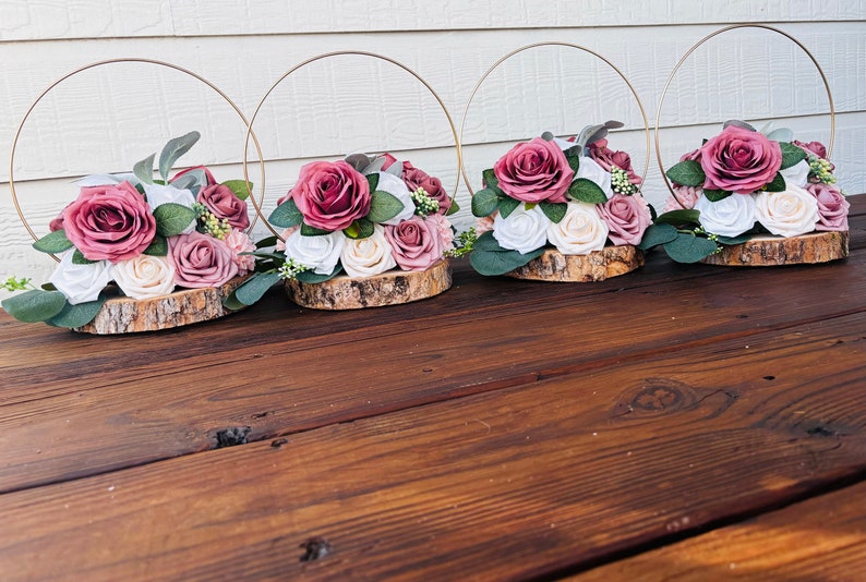 May include: Four rustic wooden centerpieces with gold hoops and pink and white artificial flower arrangements.