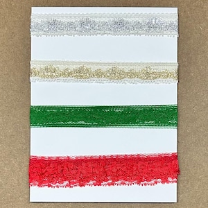 May include: Four strips of decorative lace trim arranged horizontally on a white rectangular card. The top strip is silver, the second is gold, the third is a solid forest green, and the bottom strip is a vibrant red with a scalloped edge.