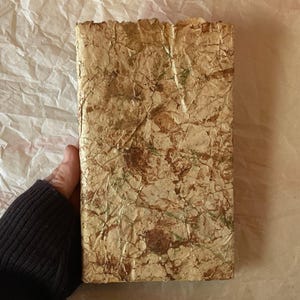 May include: A handmade journal with a textured cover made of recycled paper. The cover has a marbled pattern in shades of brown, green, and gold.