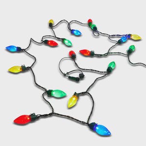 May include: A string of decorative holiday lights featuring multi-colored bulbs in red, green, blue, and yellow. The bulbs are attached to a dark green wire, with each light housing a small clip for mounting. The strand includes a connector plug.