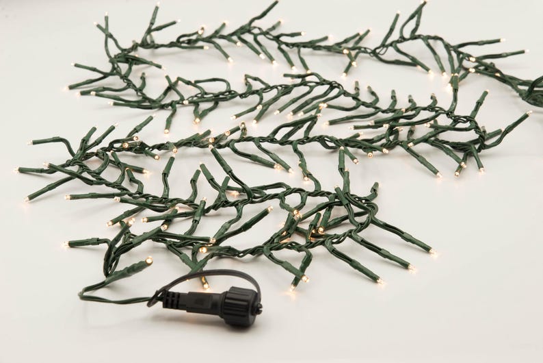 Op de afbeelding: Een string met warm witte kerstverlichting met groene draad. De lampjes zijn in een willekeurig patroon geregen en zijn perfect voor het versieren van een huis of feest.