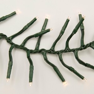 Op de afbeelding: Een string met witte kerstverlichting met groene draad. De lampjes zijn gelijkmatig verdeeld over de draad en zijn aan.