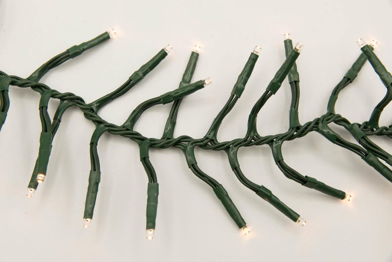 Op de afbeelding: Een string met witte kerstverlichting met groene draad. De lampjes zijn gelijkmatig verdeeld over de draad en zijn aan.