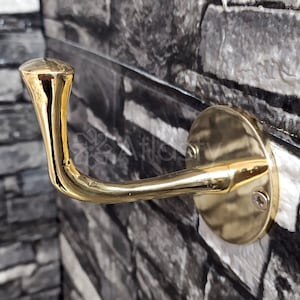 Könnte beinhalten: Ein goldfarbener Haken aus Metall mit abgerundeter Oberseite und einem gebogenen Arm. Der Haken ist auf einem runden Sockel mit einer Schraube montiert.