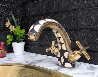 May include: A black and white patterned faucet with gold accents, mounted on a white countertop next to a gold oval sink.